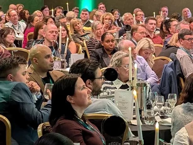 Attendees seated at round tables listening to a speaker on stage
